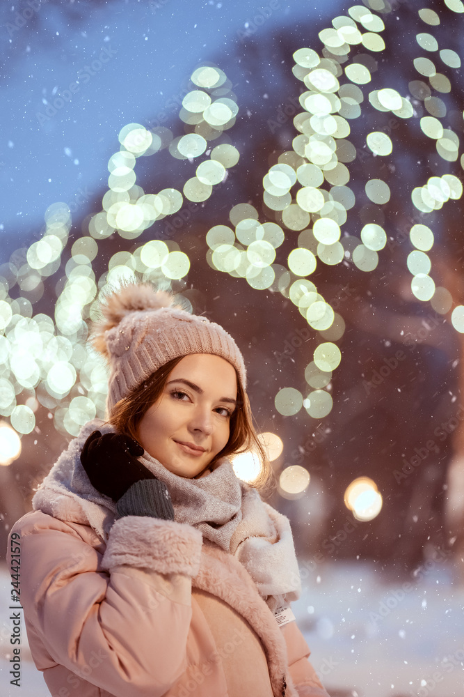 Winter portrait of smiling beautiful girl in light scarf hat and gloves under the snow. Pretty young model standing and looking at camera. Winter portrait of smiling beautiful girl in light scarf hat and gloves under the snow. Pretty young model standing and looking at camera.