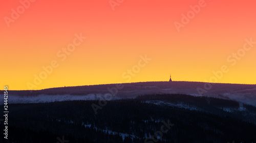 Beautiful sunset with wooden and snowy mountains with transmitter tower on the highest peak and colorful golden red sky, Cerna hora (Schwarzenberg), Krkonose (Giant Mountains), Czech Republic