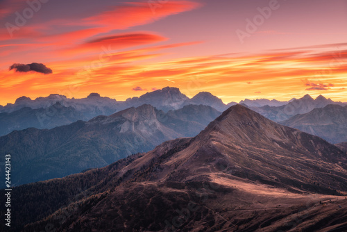 Mountains at beautiful sunset in autumn in Dolomites, Italy. Landscape with rocks, forest on hills and orange sky with red clouds in the evening. Autumn scenery with mountain valley. Italian alps
