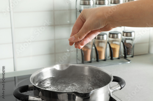 Woman salting boiling water in pot on stove, closeup