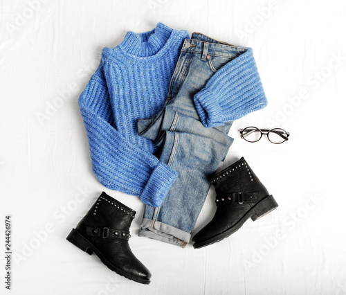 Flat lay composition with jeans, sweater and shoes on white fabric
