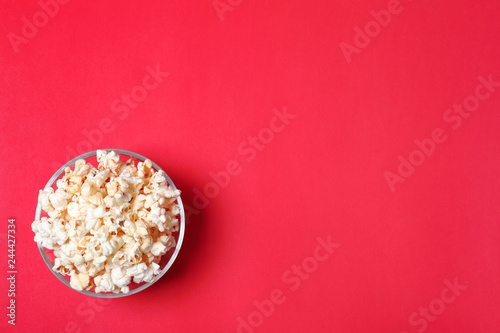 Glass bowl with tasty popcorn on color background, top view. Space for text