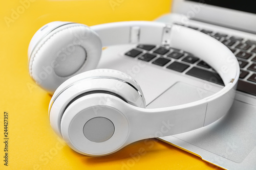 Modern headphones and laptop on color background, closeup