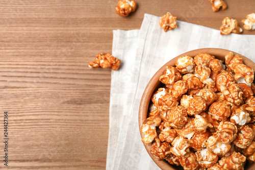 Bowl with caramel popcorn on wooden background, top view. Space for text