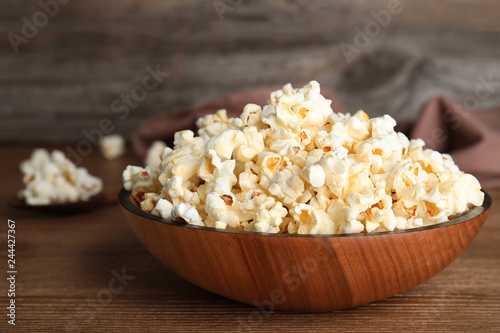 Wooden bowl with tasty popcorn on table