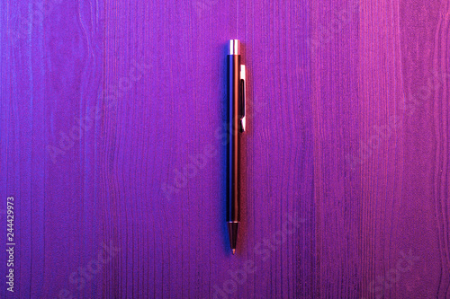 Elegant pen on wood background and purple and pink light. Business black pen. Top view