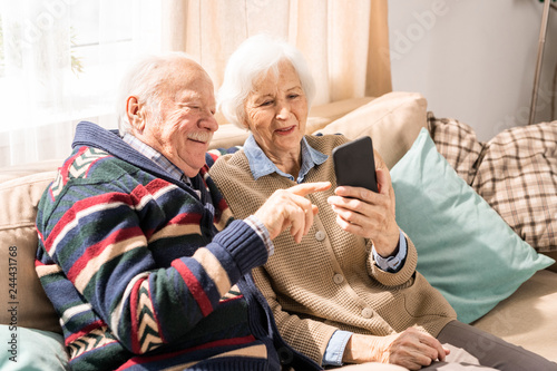 Portrait of adorable senior couple using smartphone together video chatting with family at home, copy space