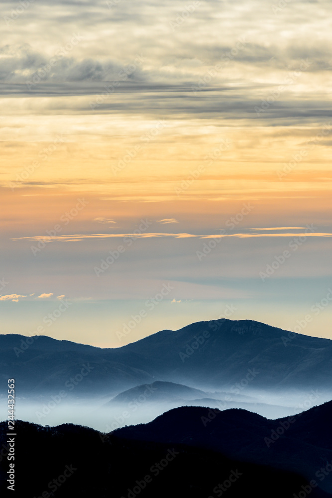 Beautiful view of some mountains surrounded by clouds and fog during sunset. National Park of Abruzzo, Lazio and Molise, Italy.