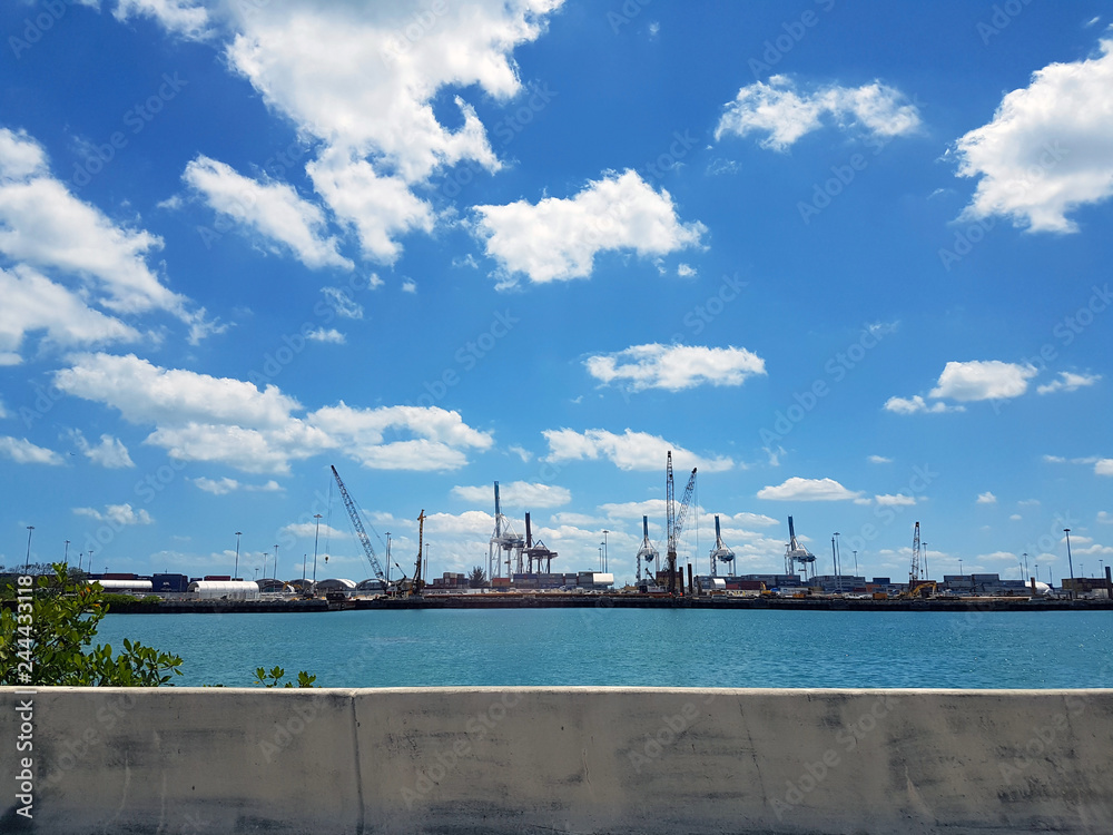 Cargo port in Miami view from a passing car on the highway in clear weather. Cranes at the seaport in florida through concrete railing Cargo port in Miami view from a passing car on the highway in clear weather. Cranes at the seaport in florida through concrete railing