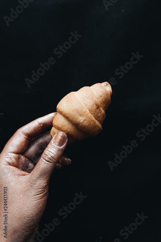 Female hand holding small croissant over black background
