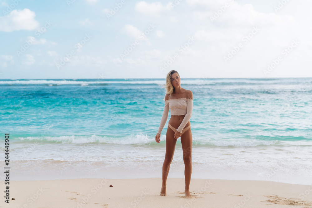 Beautiful tanned girl standing on beach with white sand and blue ocean