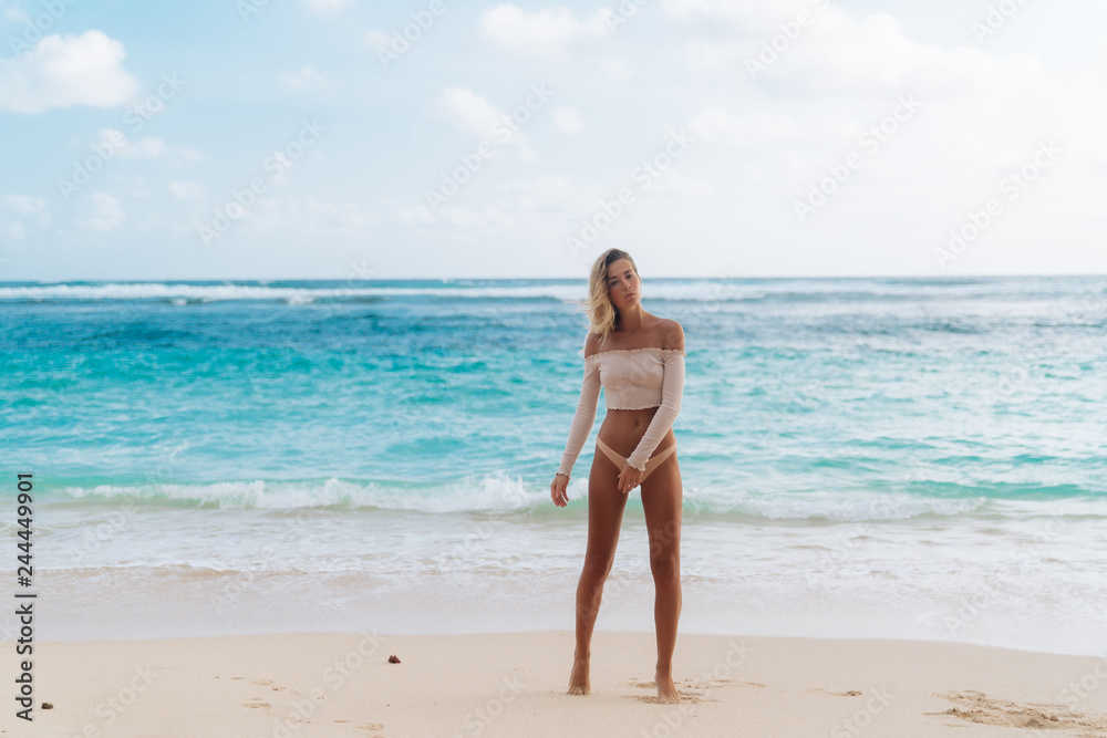 Beautiful tanned girl standing on beach with white sand and blue ocean Beautiful tanned girl standing on beach with white sand and blue ocean
