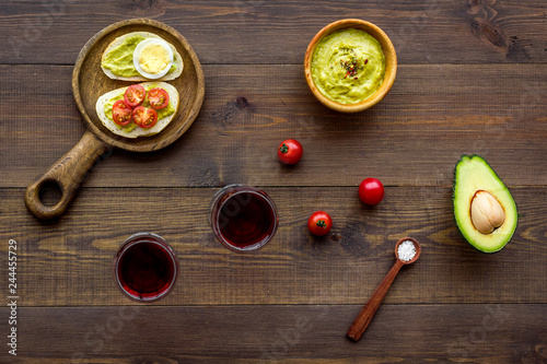 Light appetizer with avocado. Toasts with vegetables and guacamole near glasses of wine on dark wooden background top view