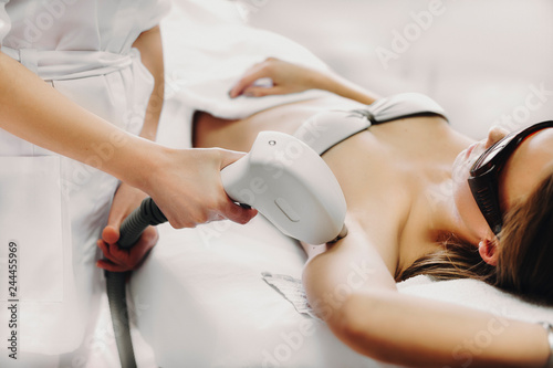 Professional doctor doing laser epilation to a young woman in a salon. photo