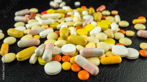 Multi-colored pills and capsules scattered on the table on a dark background
