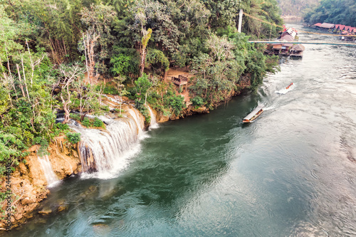 Wooden boat sailing river kwai with waterfall in tropical rainforest photo