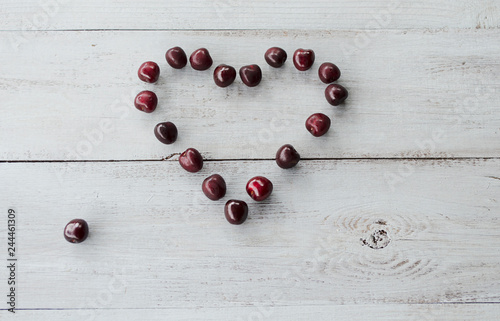 red sweet cherry laid out on a light wooden background in the form of heart 
