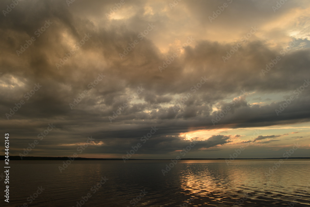 Dramatic sky above the water of a lake in the sunlight from a cloud at sunset