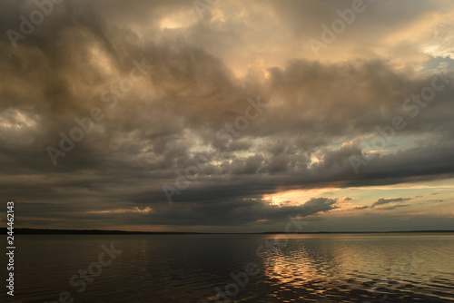 Dramatic sky above the water of a lake in the sunlight from a cloud at sunset