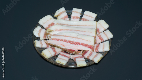 Salted bacon with pepper, garlic and spices on the plate and black background