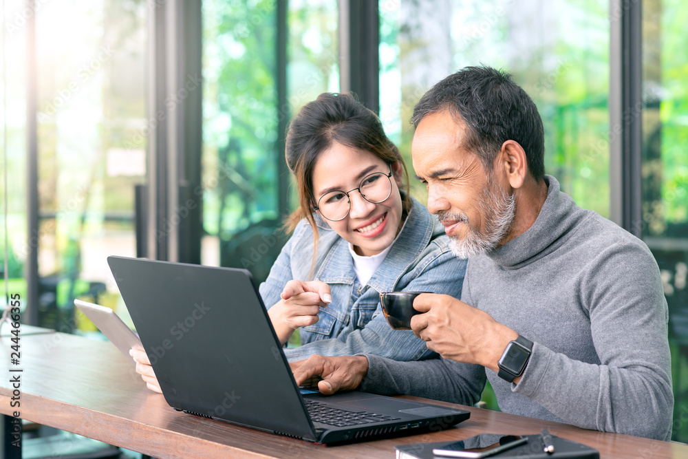 Attractive mature asian man with white stylish short beard looking at laptop computer with teenage eye glasses hipster woman in cafe. Teaching internet online or wifi technology in older man concept. Attractive mature asian man with white stylish short beard looking at laptop computer with teenage eye glasses hipster woman in cafe. Teaching internet online or wifi technology in older man concept.
