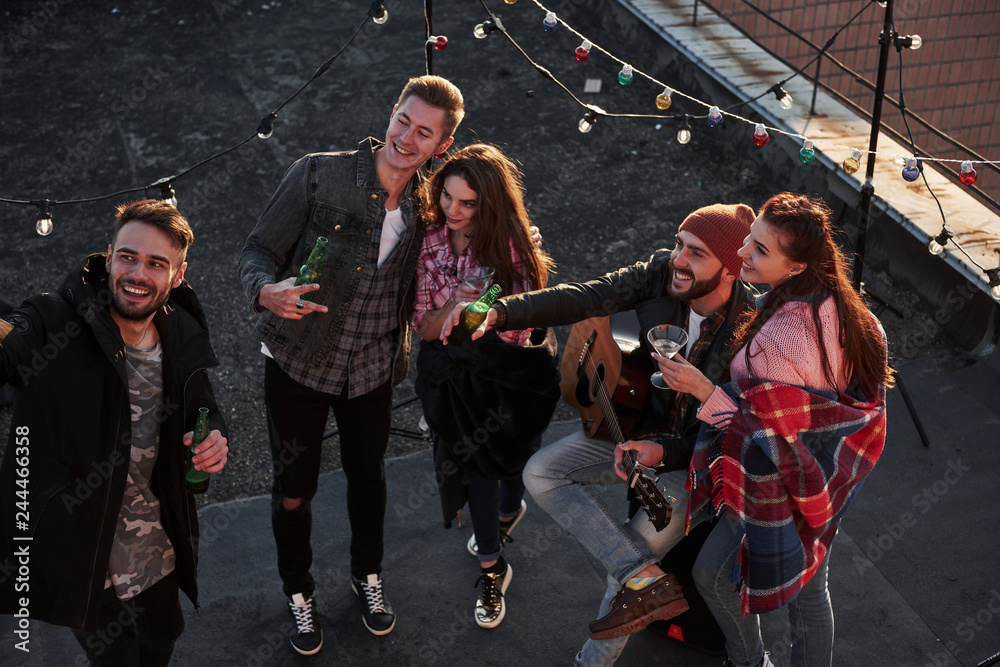 Fototapeta premium Finally they met. Top view of a young friends that take selfie while have fun at the roof with decorative colorful light bulbs