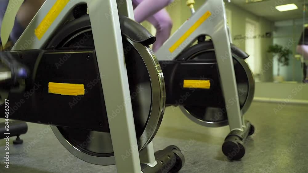Close-up of women's legs riding a stationary bike in the gym. Close-up of women's legs riding a stationary bike in the gym.
