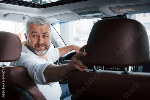 Cheerful mood. Driving a car in reverse gear. Looking behind. Man in his brand new automobile photo