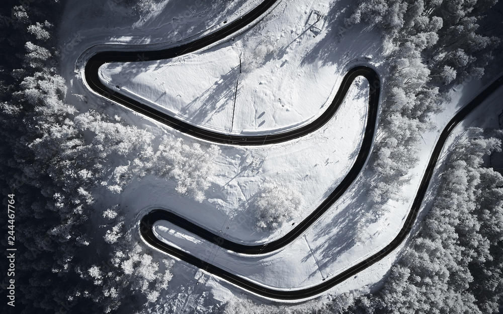 Aerial drone view of a curved winding road through the forest high up in the mountains in the winter with snow covered trees