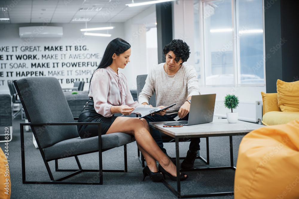 Curly guy and brunette girl discusses the details of the contract in modern office Curly guy and brunette girl discusses the details of the contract in modern office