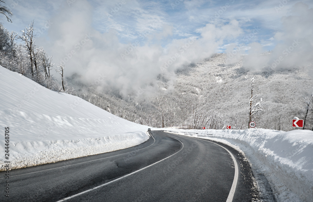 Aerial drone view of a curved winding road through the forest high up in the mountains in the winter with snow covered trees Aerial drone view of a curved winding road through the forest high up in the mountains in the winter with snow covered trees