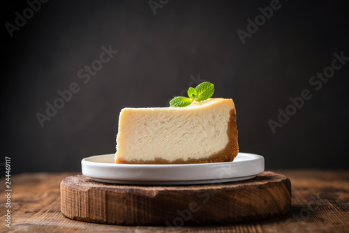 Slice of cheesecake with mint leaf on wooden cake stand over black background. Copy space for text photo