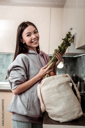 Appealing cheerful family woman holding celery in the kitchen