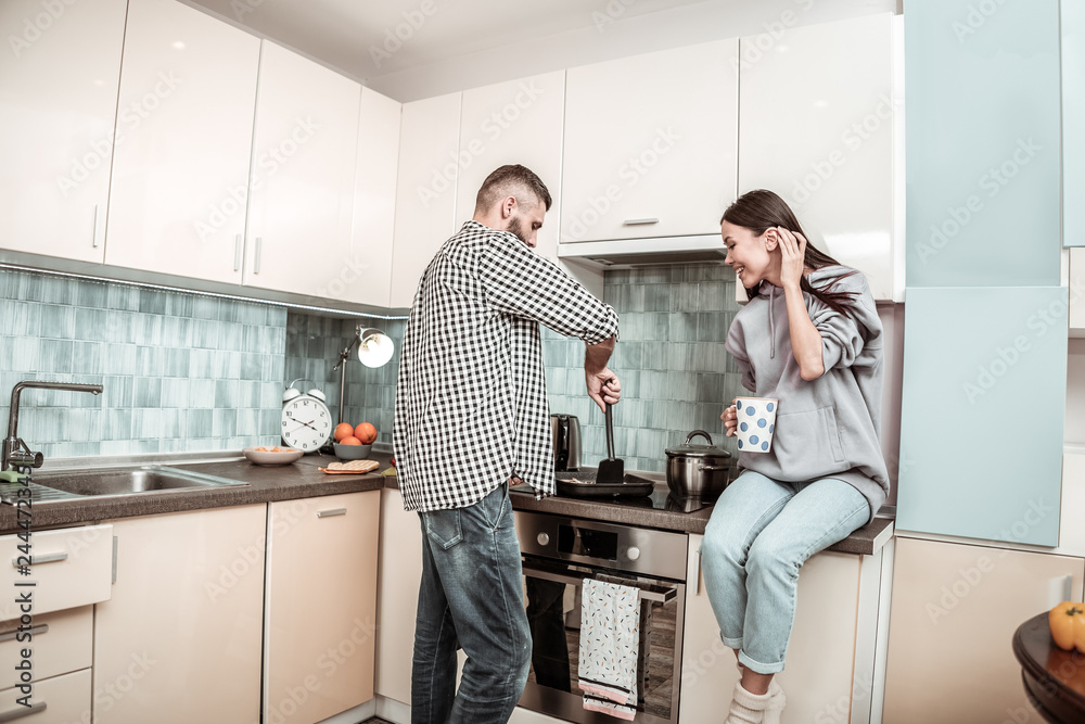 Appealing wife sitting near cooker while her husband cooking Appealing wife sitting near cooker while her husband cooking