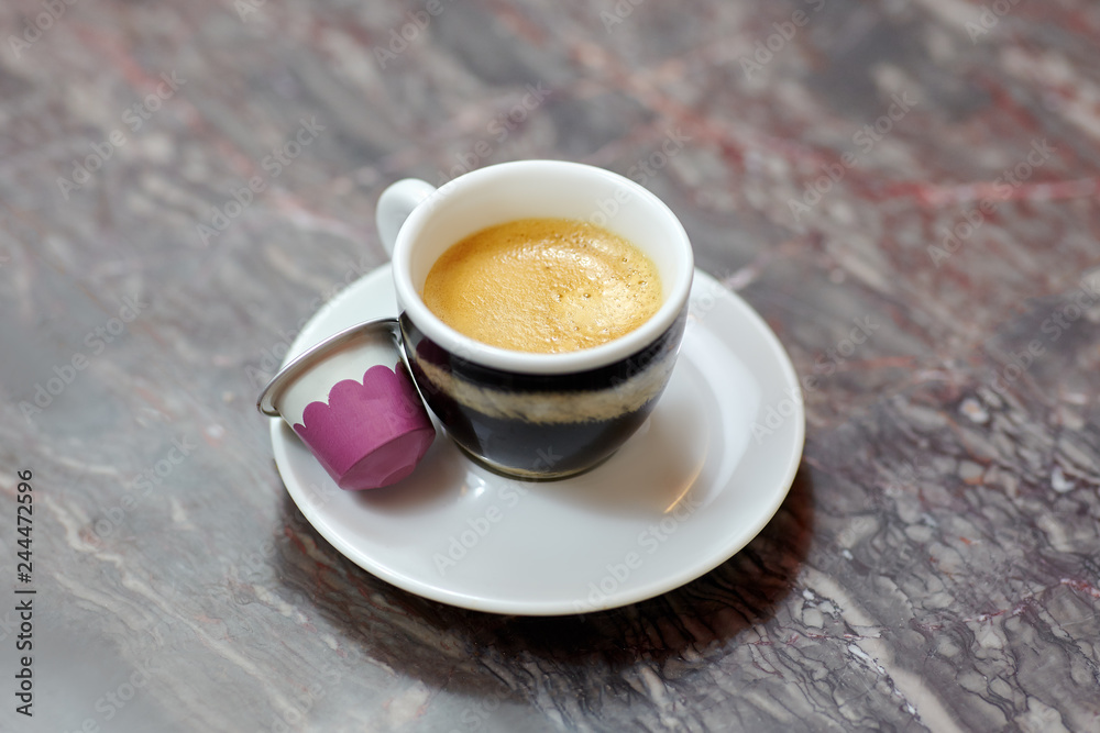 Close up picture of little cup and saucer, with coffee espresso, with tiger pattern design, on marble background. White and pink replaceable cartridge from coffee on the saucer. Indoors, copy space. Close up picture of little cup and saucer, with coffee espresso, with tiger pattern design, on marble background. White and pink replaceable cartridge from coffee on the saucer. Indoors, copy space.