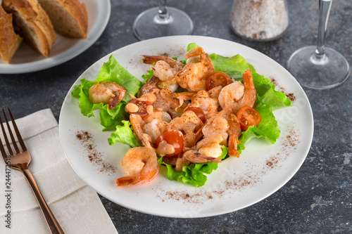 salad with Royal prawns on a white plate on the dark surface of the table with Cutlery.