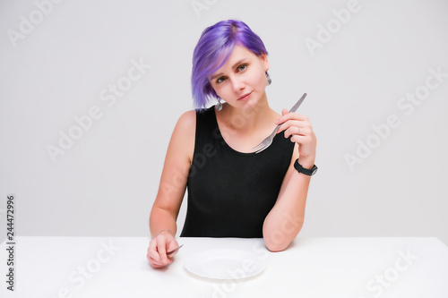 Fork  plate  knife - Concept portrait of a beautiful girl with purple hair on a white background sitting at a table with dining tools.