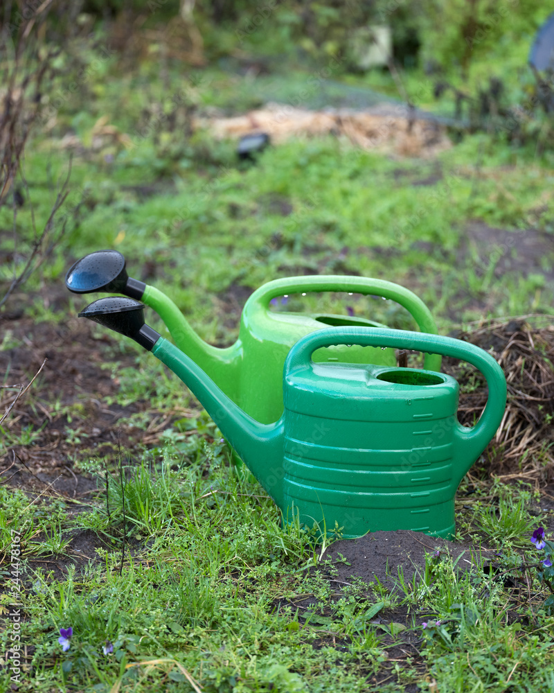 two green watering cans on soil of garden two green watering cans on soil of garden