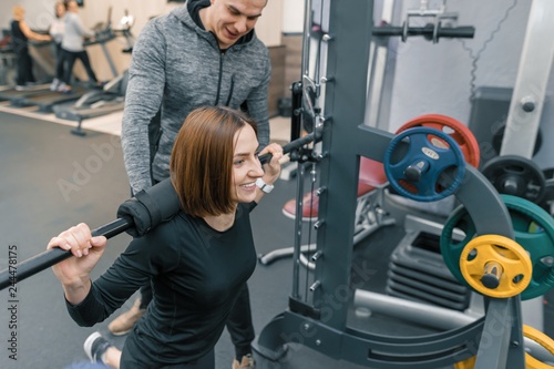 Male personal fitness trainer helping young woman to do workout in gym. Sport, athlete, training, healthy lifestyle and people concept