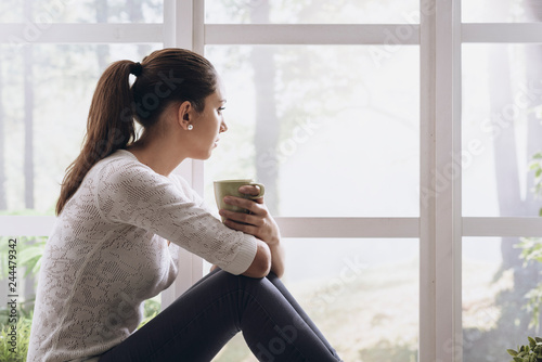 Tableau sur toile Young woman sitting next to the window and looking away