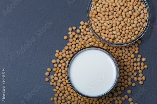 Top view of soy seeds and glass of milk on slate background.