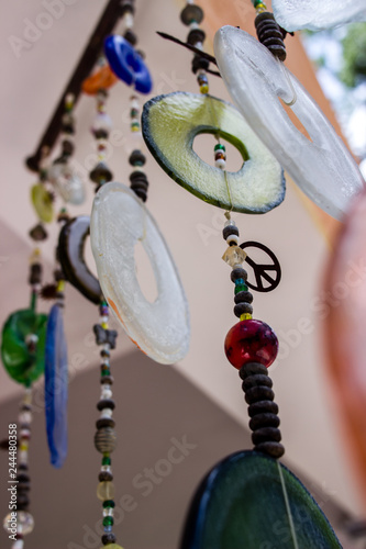 Close up of various wind chimes made out of recycled plastic, glass and metal objects with a peace symbol (ID: 244480358)