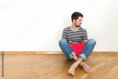 Canvas Print Happy valentines day! Young man is sitting on the floor with red heart and smiling