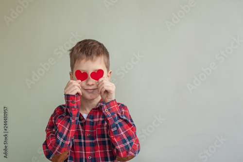 Cute sweet boy holding red love hearts over eyes.