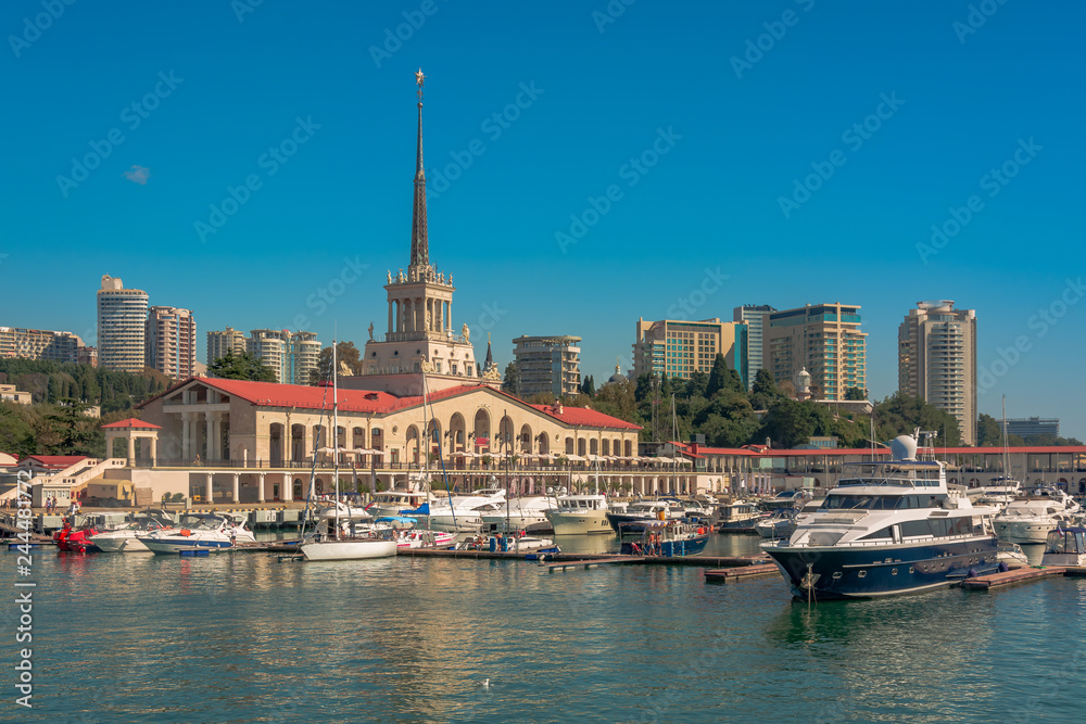 Fototapeta premium Sea port in summer. Many different yachts and boats stand at the marina. Yachtsmen and travelers are preparing to sail in the sea. In the background of the building of the seaside city.