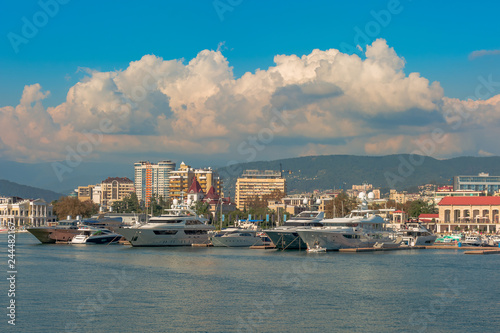 Sea port in summer. Many different yachts and boats stand at the marina. Yachtsmen and travelers are preparing to sail in the sea. In the background of the building of the seaside city.