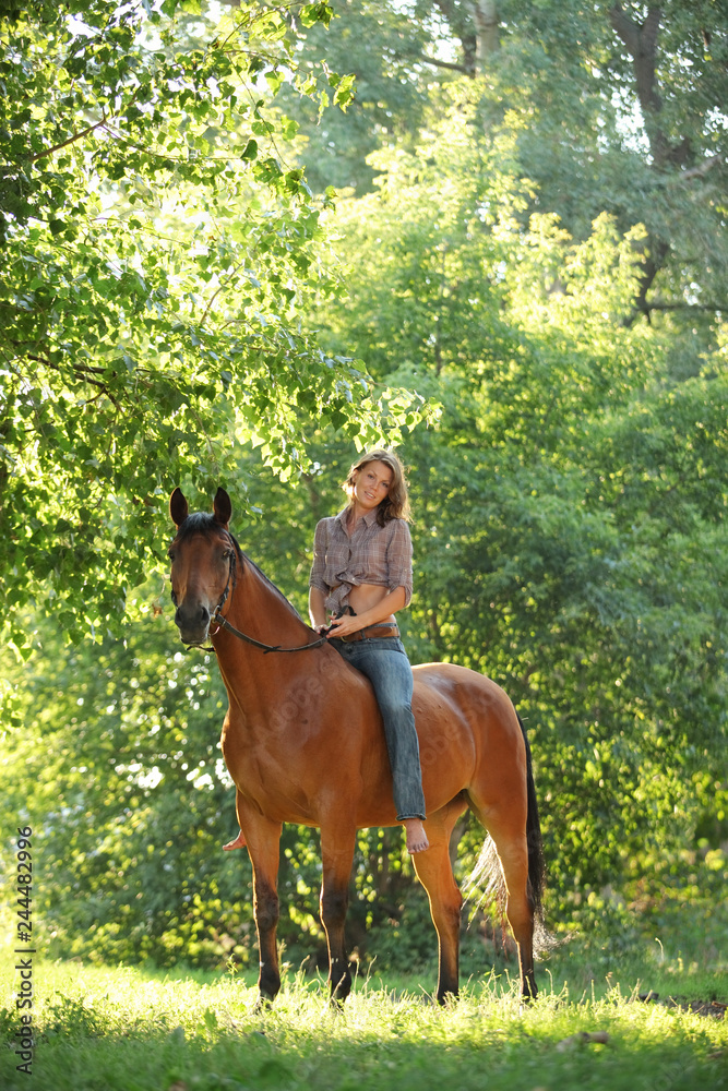 Fototapeta premium Beautiful cowgirl bareback ride her horse in woods glade at sunset