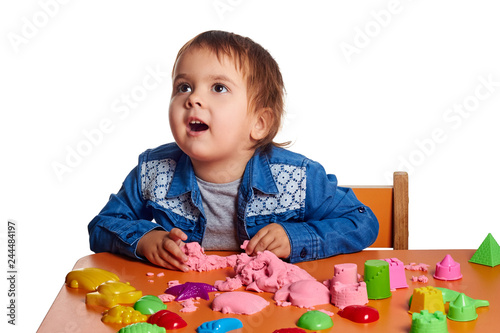 Emotional little child girl playing with kinetic sand on the orange table. Isolated white background