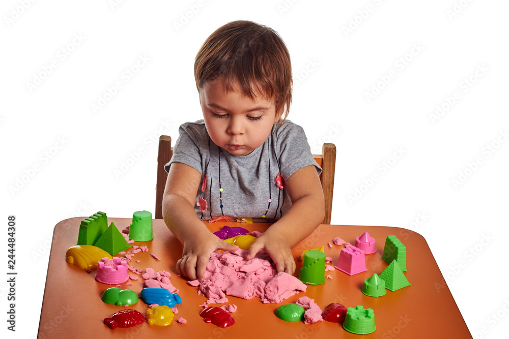 Emotional little child girl playing with kinetic sand on the orange table. Isolated white background Emotional little child girl playing with kinetic sand on the orange table. Isolated white background