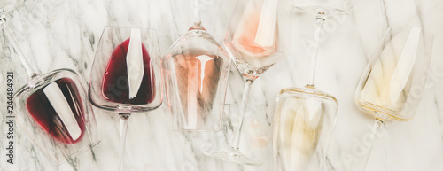 Flat-lay of red, rose and white wine in glasses and corkscrews over grey marble background, top view, wide composition. Wine bar, winery, wine degustation concept